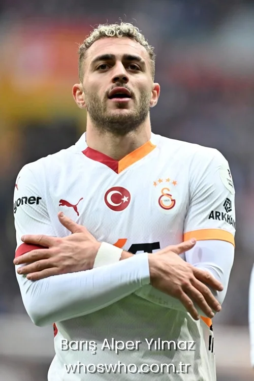 Turkish international football player Baris Alper Yilmaz with blonde-tipped hair, wearing the white Galatasaray jersey and crossing his arms across his chest during a match celebration.