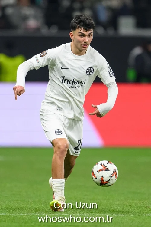Young Turkish midfielder Can Uzun controlling the soccer ball on the pitch during a match, wearing the white Eintracht Frankfurt jersey with the Indeed sponsor logo.