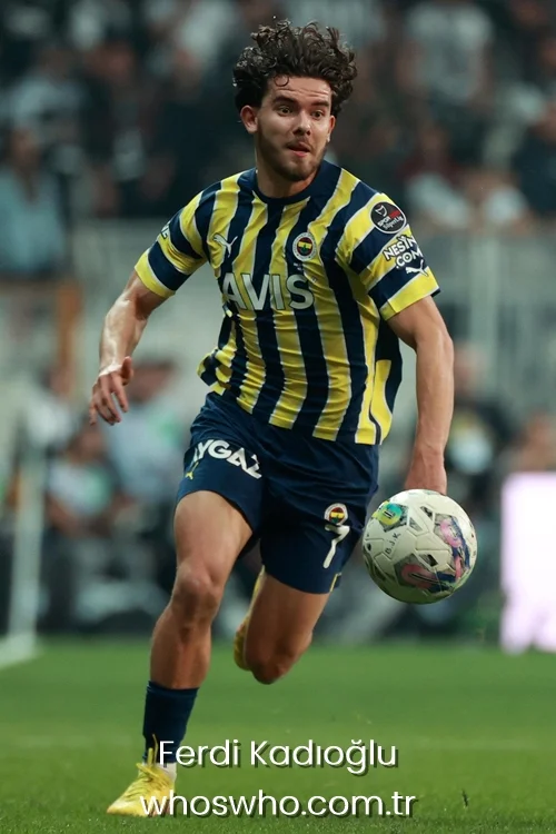 Turkish fullback Ferdi Kadioglu with curly hair dribbling a soccer ball during a match, wearing the yellow and navy blue striped Fenerbahce jersey and blue shorts.