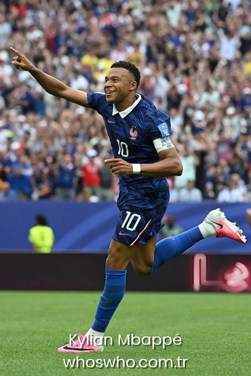 French striker Kylian Mbappé running and smiling while pointing forward during a goal celebration in the classic blue France national team kit.