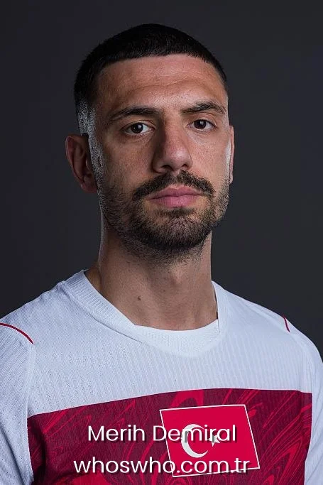 Close-up studio portrait of Turkish defender Merih Demiral with short hair and a beard, wearing the white and red Turkey national football team jersey against a dark background.