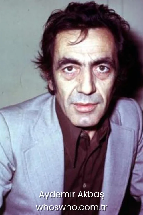 Young Aydemir Akbas posing for a portrait in a grey blazer and brown shirt. 