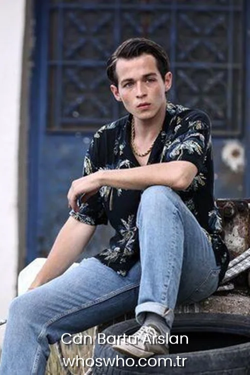 Can Bartu Arslan wearing a patterned shirt and jeans sitting on a tire.