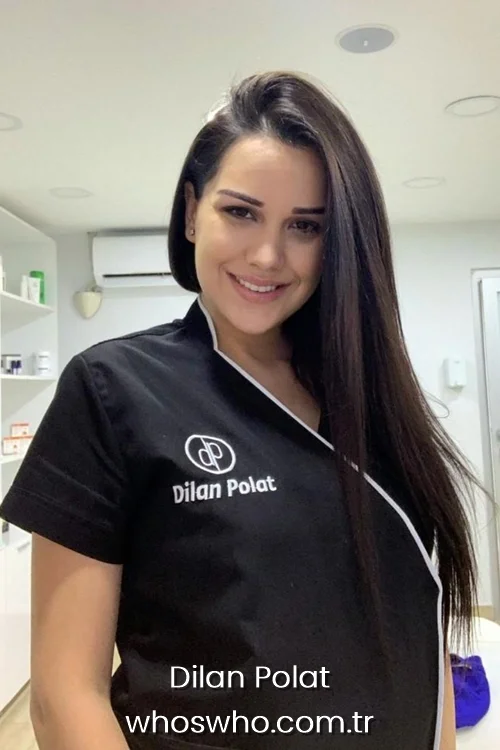 Smiling Turkish entrepreneur Dilan Polat with long straight dark hair, wearing a black beauty clinic uniform with the Dilan Polat logo, posing inside a brightly lit aesthetics clinic.