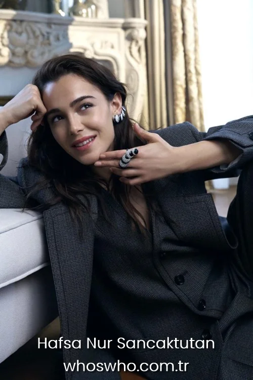 Hafsanur Sancaktutan in a grey plaid suit wearing diamond earrings and a ring.