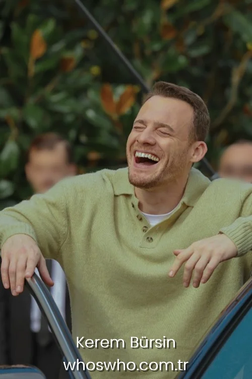 Kerem Bursin laughing out loud wearing a green knit polo shirt.