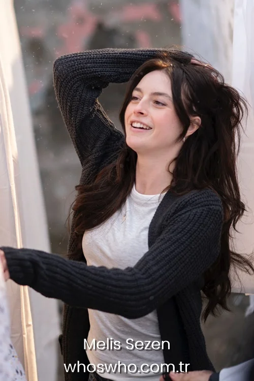 Turkish actress Melis Sezen smiling outdoors, wearing a dark knit cardigan over a white t-shirt