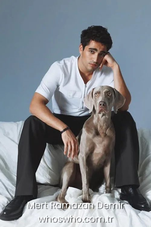 Mert Ramazan Demir sitting on a white sheet draped couch with a Weimaraner dog.