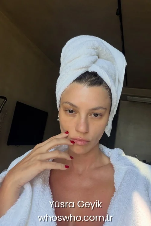 Turkish actress Yusra Geyik without makeup wearing a white bathrobe and a towel wrapped around her hair indoors