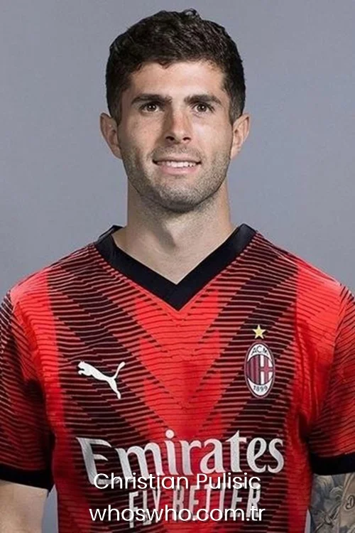 Christian Pulisic smiling for a headshot portrait wearing the red and black AC Milan jersey.