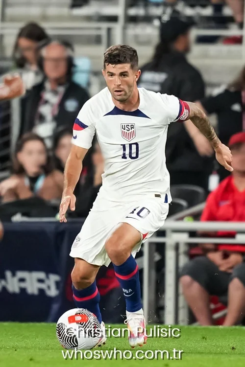 Christian Pulisic dribbling a soccer ball on the pitch wearing USMNT jersey number 10 and a captain armband.