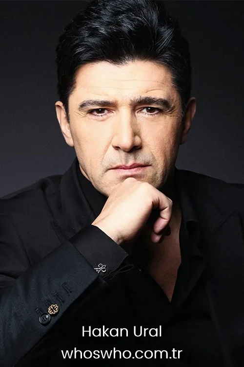 Hakan Ural posing for a portrait in a black suit with his hand on his chin.