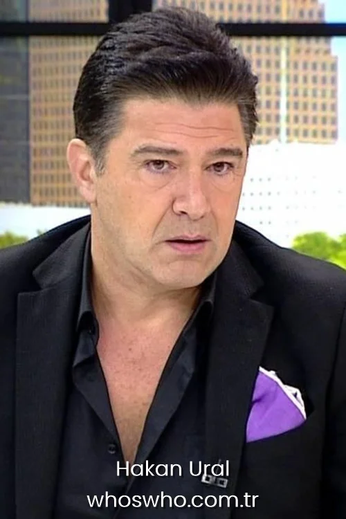 Hakan Ural wearing a black suit with a purple pocket square on a TV studio set.