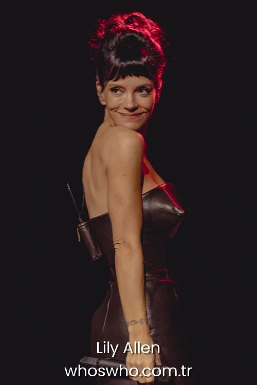 Singer Lily Allen looking over her shoulder on stage wearing a strapless black leather dress.