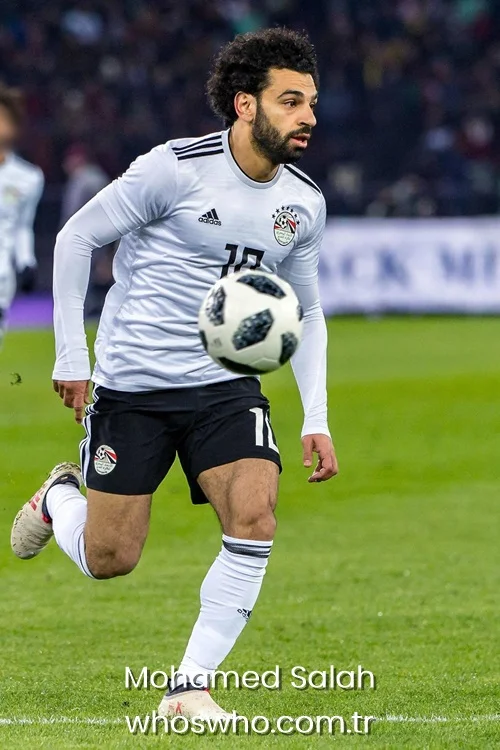 Egyptian forward Mohamed Salah sprinting on the pitch while controlling a soccer ball in the official white Egypt national team kit during an international match.