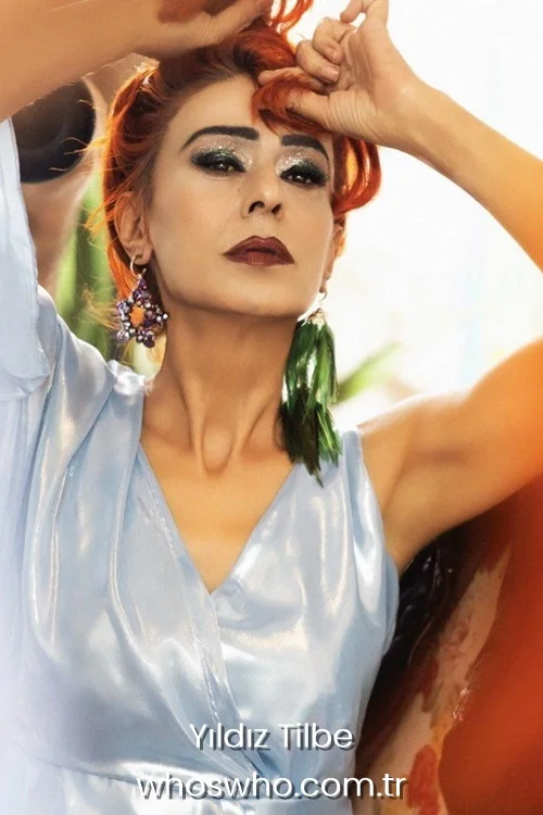 Yildiz Tilbe with dramatic silver glitter eyeshadow and red hair wearing a shiny blue satin dress.