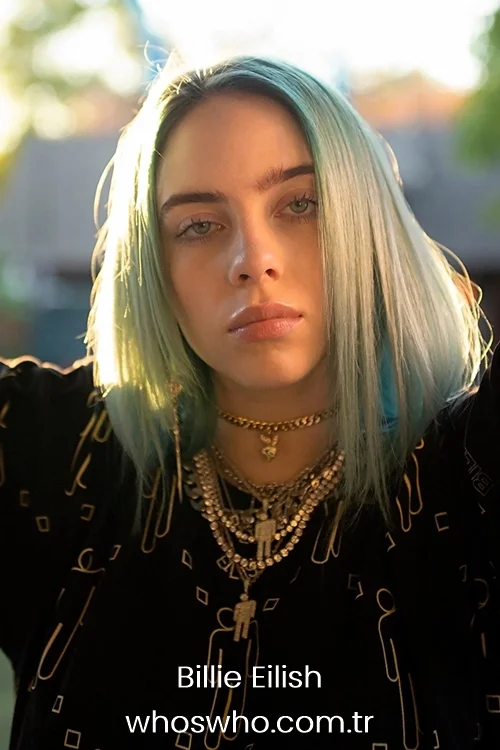 Billie Eilish with pastel blue hair wearing layered chain necklaces.
