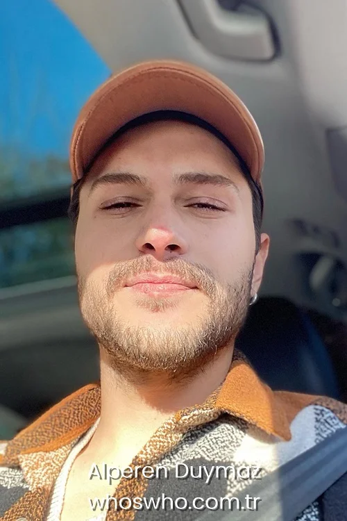 Alperen Duymaz taking a sun-kissed selfie inside a car wearing a brown cap.