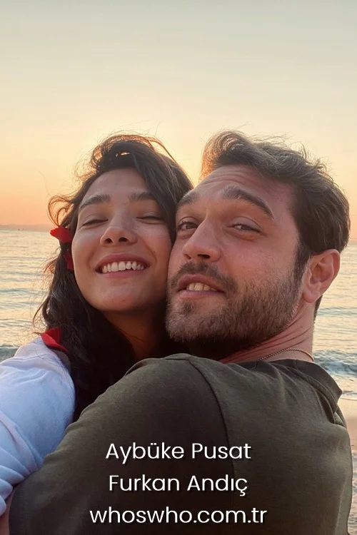 Romantic sunset portrait of Turkish actors Aybuke Pusat and Furkan Andic hugging by the sea, with Aybuke smiling warmly next to Furkan on a sandy beach background.