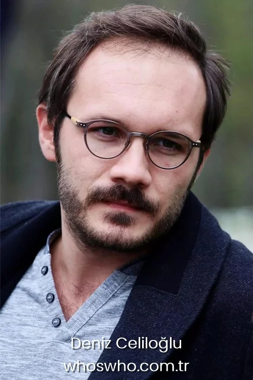 Close-up portrait of Turkish actor Deniz Celiloglu with a beard and mustache, wearing round eyeglasses, a grey buttoned t-shirt, and a dark blue winter coat or jacket.
