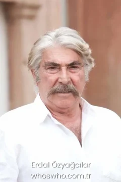 Turkish actor Erdal Ozyagcilar with white hair and a thick mustache wearing a white button-up shirt looking at the camera