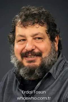 Close-up studio portrait of smiling Turkish actor Erdal Tosun with a grey-streaked beard.