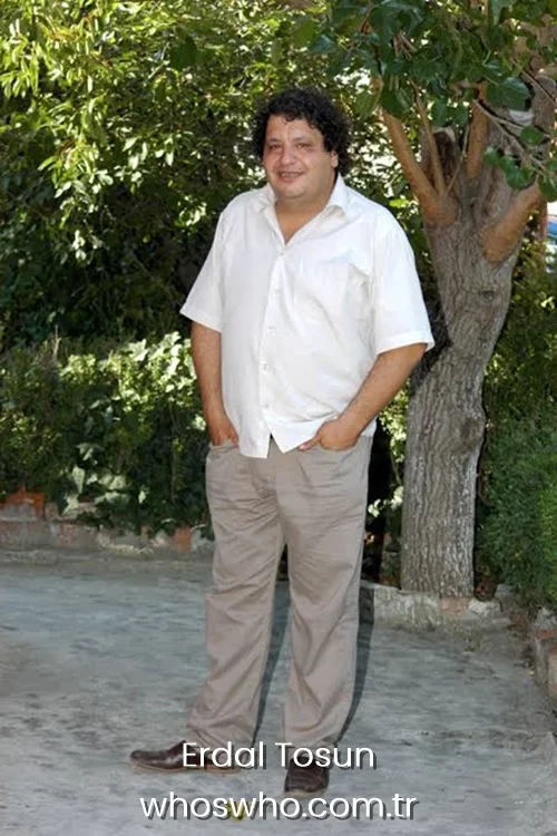Turkish actor Erdal Tosun posing outdoors in a white short-sleeve button-down shirt and beige trousers.
