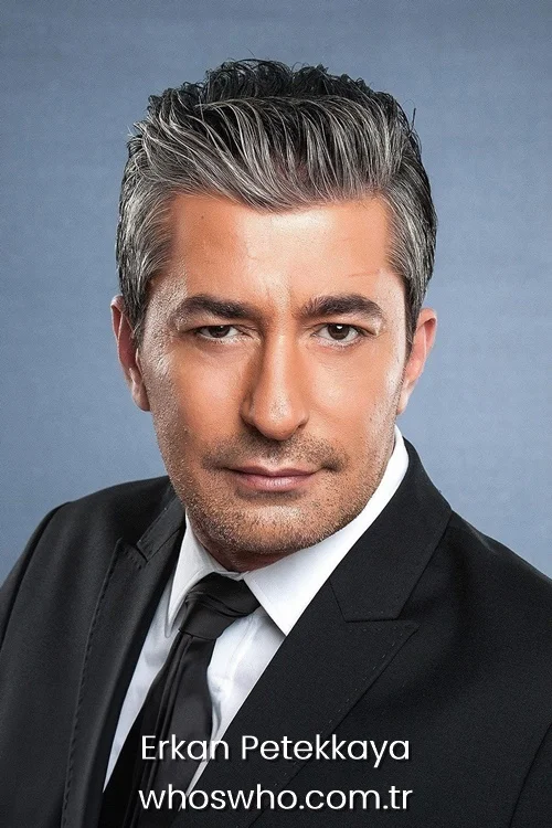 Close-up portrait of Turkish actor Erkan Petekkaya with graying hair, wearing a classic black suit and black tie against a gray background.