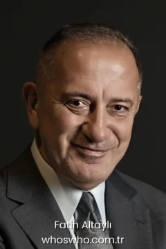 Turkish journalist Fatih Altayli smiling while wearing a grey suit and a matching tie against a dark background