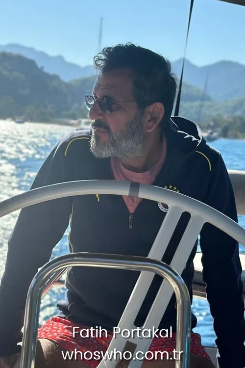 Turkish journalist Fatih Portakal wearing sunglasses and steering a boat on the sea with scenic mountains behind.
