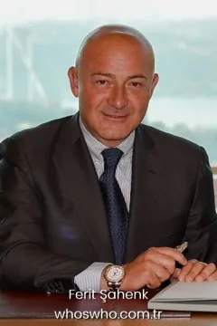 Turkish businessman Ferit Şahenk smiling in a dark suit and blue tie sitting at his desk.
