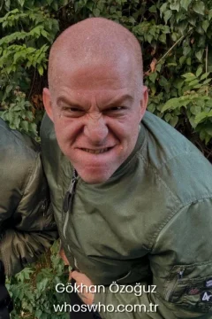 Turkish musician Gokhan Ozoguz with a shaved bald head making an aggressive facial expression wearing a green bomber jacket outdoors