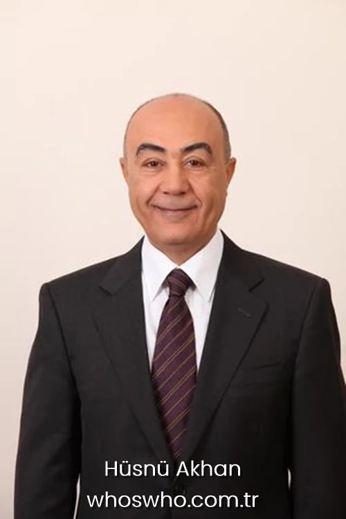 Turkish business executive Hüsnü Akhan smiling in a classic black suit and striped tie against a plain background.