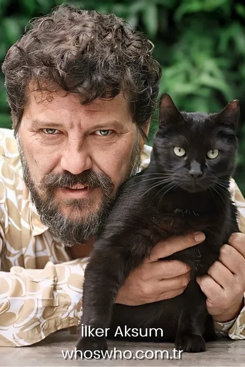 Turkish actor Ilker Aksum with a beard holding a black cat in his hands outdoors with green plants background