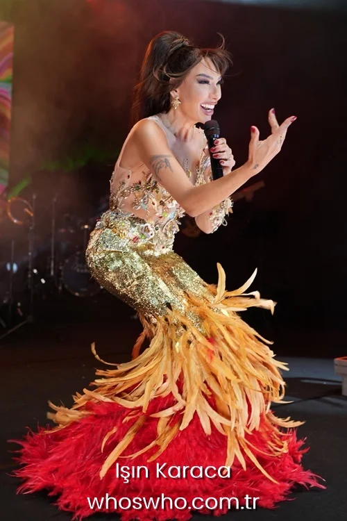 Turkish pop star Işın Karaca singing into a microphone on stage in a gold sequin and red feathered dress.