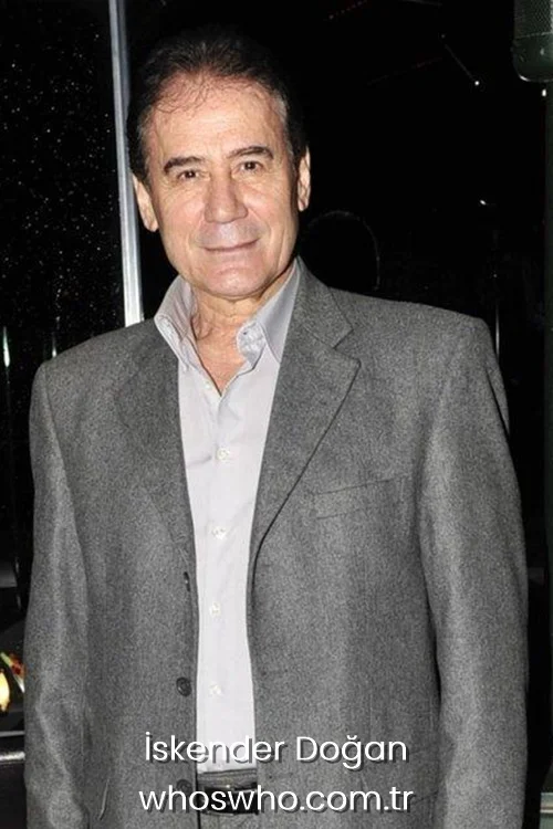 Turkish pop singer İskender Doğan smiling while wearing a grey suit jacket and light grey shirt.