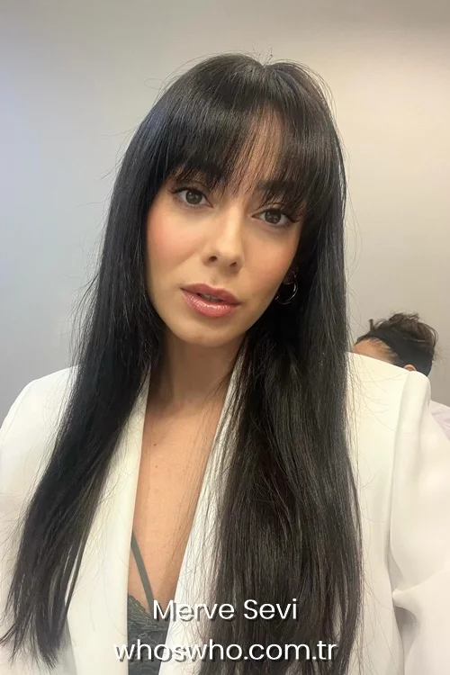 Close-up portrait of Turkish actress Merve Sevi with long dark hair and bangs, wearing a white blazer.