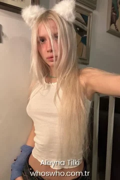 Turkish pop singer Aleyna Tilki with long blonde hair posing for a casual selfie wearing a white fluffy cat ears headband and a ribbed tank top