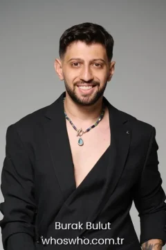 Turkish pop singer Burak Bulut smiling in a black blazer jacket and wearing a blue gemstone pendant necklace