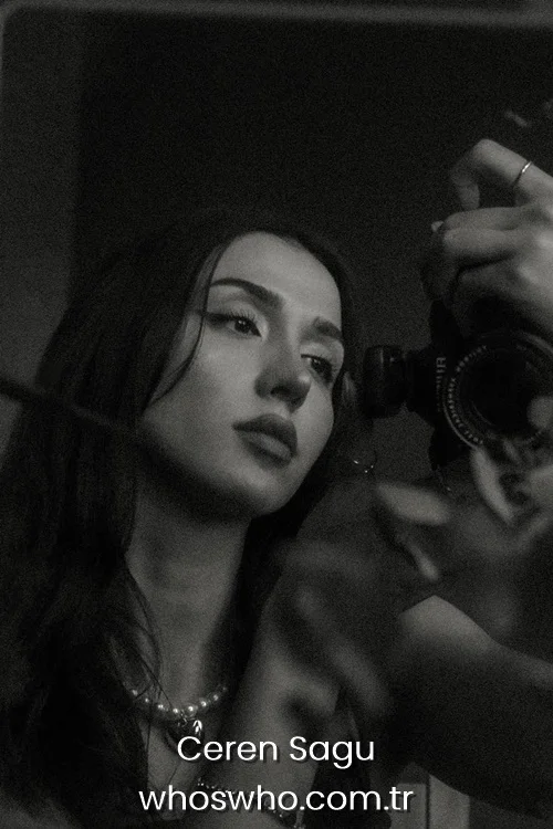 Turkish pop singer Ceren Sagu posing for a dramatic black and white mirror selfie while holding a professional camera and wearing a pearl necklace 