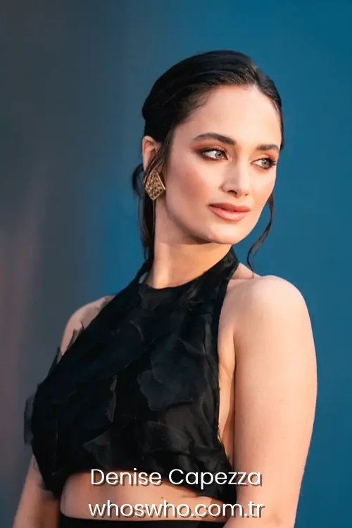 Actress Denise Capezza showcasing her side profile in a black halter neck top and gold earrings.