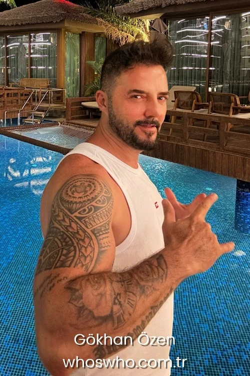 Singer Gokhan Ozen showing his arm tattoos by a luxury swimming pool.