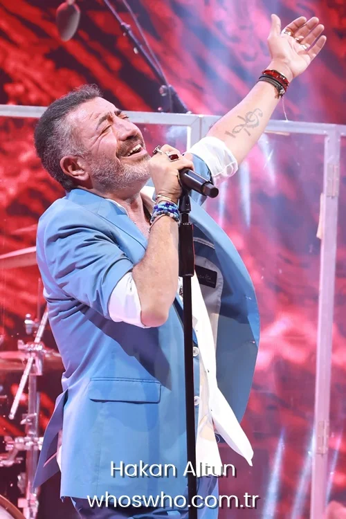 Turkish singer Hakan Altun singing on stage with his arm raised, wearing a blue suit