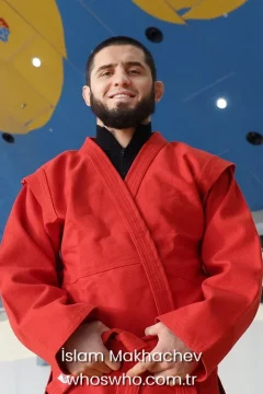 UFC fighter Islam Makhachev smiling in a red sambo uniform for his official biography profile cover.