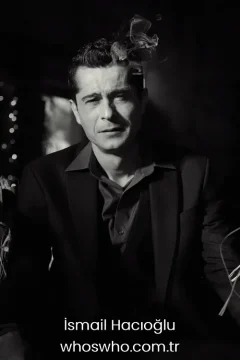 Dramatically lit black and white portrait of Turkish actor Ismail Hacioglu wearing a dark suit with smoke rising above his head