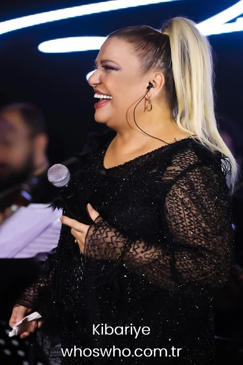 Turkish arabesque singer Kibariye laughing and singing into a microphone on stage in a black embroidered lace dress during a live concert 
