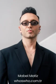 Turkish singer and songwriter Mabel Matiz portrait wearing a black suit and glasses for his official biography profile cover.