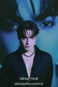 Miraç Fırat career Official close-up promotional portrait of Crush boy band member Miraç Fırat posing in an open black button-up shirt and a silver cuban link chain necklace, featuring dark hair with curtains bangs and looking directly at the camera under artistic lighting with a large projection of eyes in the blue background.
