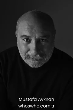 Mustafa Avkıran family A professional black and white studio headshot portrait of veteran Turkish actor Mustafa Avkıran looking directly into the camera with a subtle smile, featuring a close-cropped grey beard and mustache, wearing a dark turtleneck sweater against a dark backdrop.