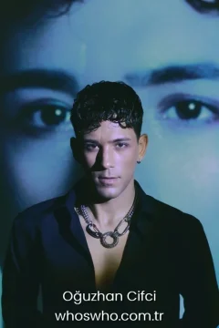 Oğuzhan Çifçi height Official close-up promotional portrait of Crush boy band member Oğuzhan Çifçi posing in a black unbuttoned shirt and a chunky silver chain necklace with a circular pendant, looking directly at the camera under artistic lighting against a dark blue background with large eyes projected.